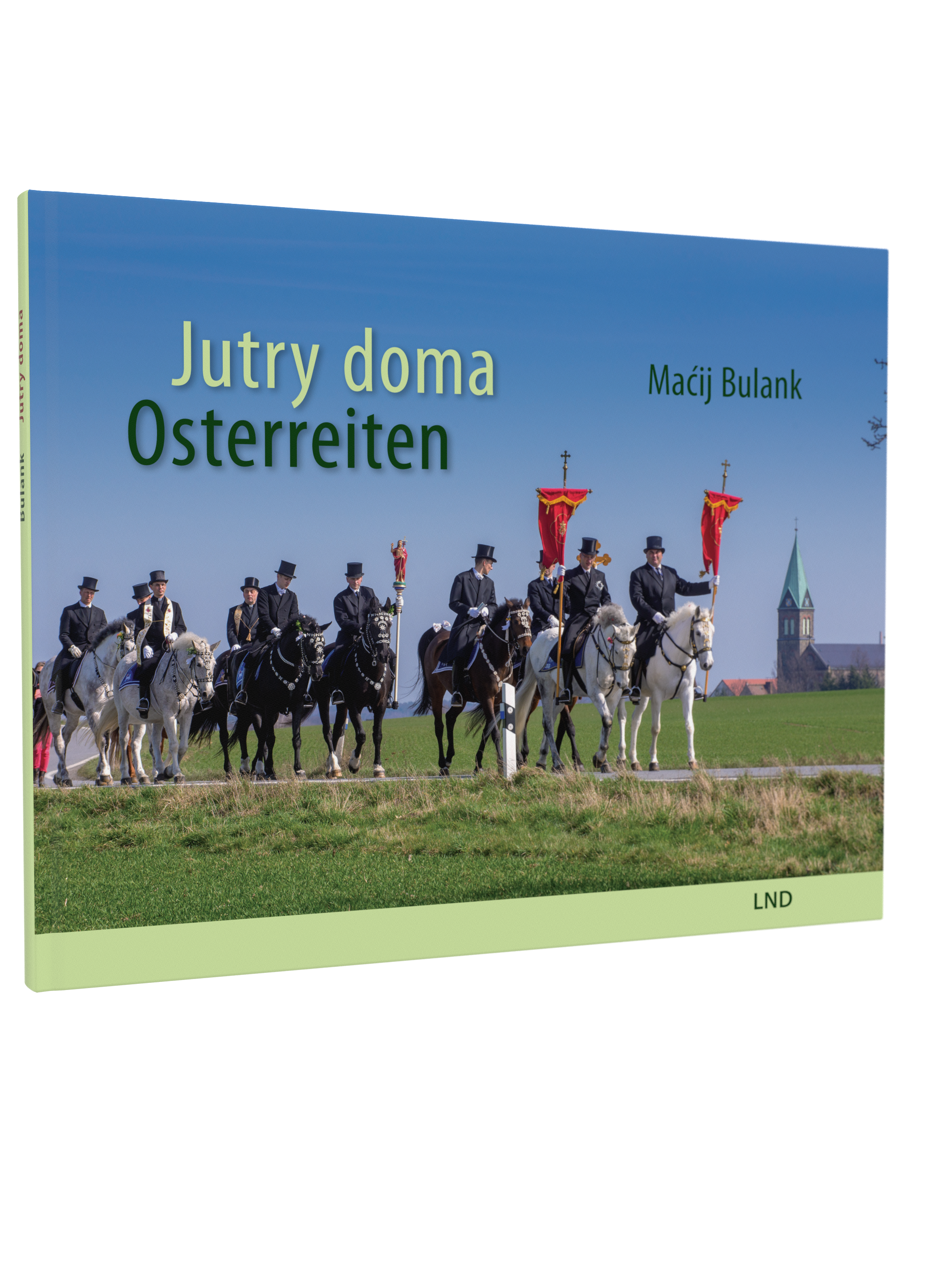 Buchcover von 'Jutry doma – Osterreiten' von Macij Bulank. Foto zeigt festlich gekleidete Reiter auf geschmückten Pferden mit roten Bannern. Sie reiten durch eine grüne Landschaft mit Kirche im Hintergrund. Titel in grüner Schrift auf blauem Himmel.